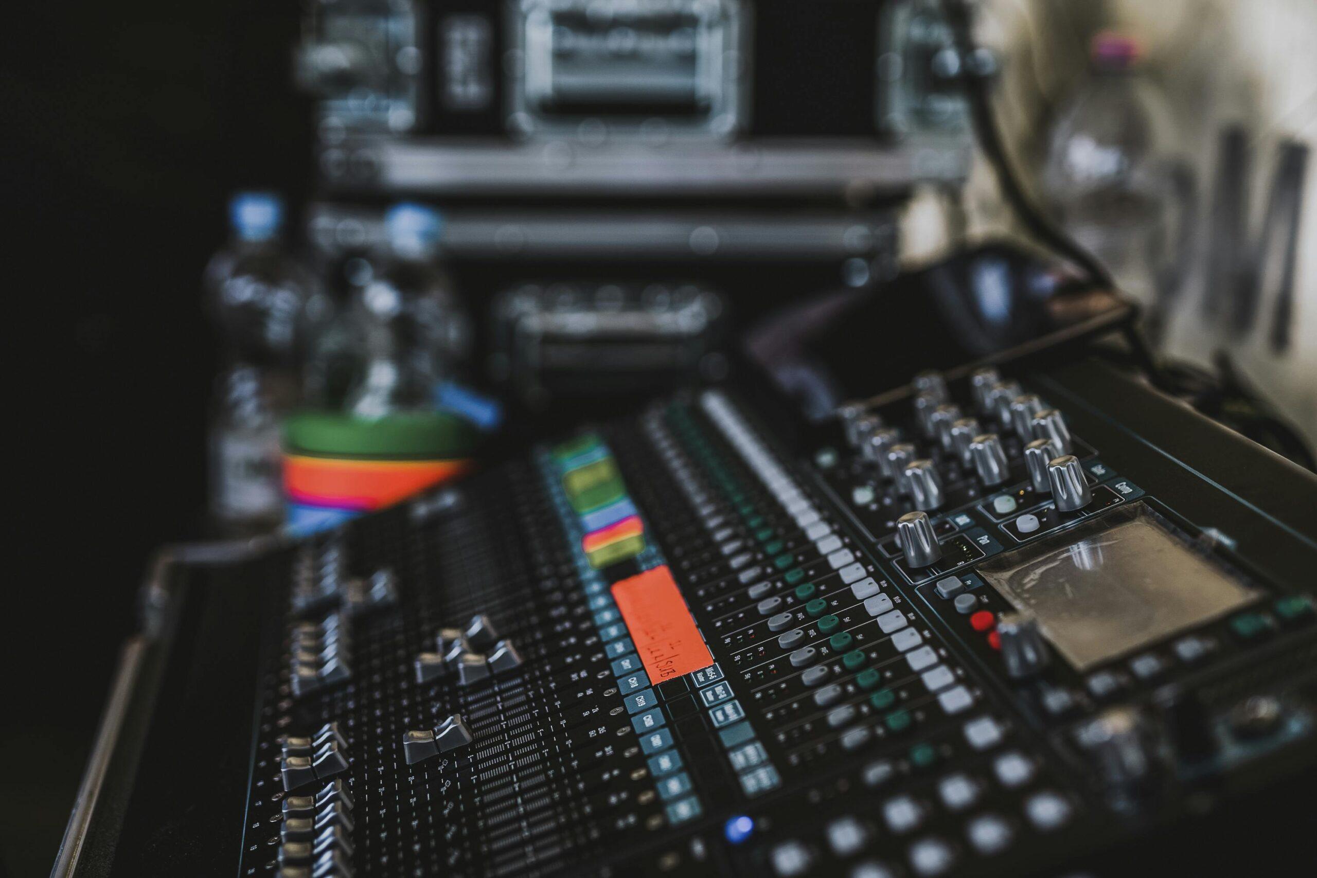 Services Close-up of a professional audio mixer with various knobs and sliders in a music studio setting.