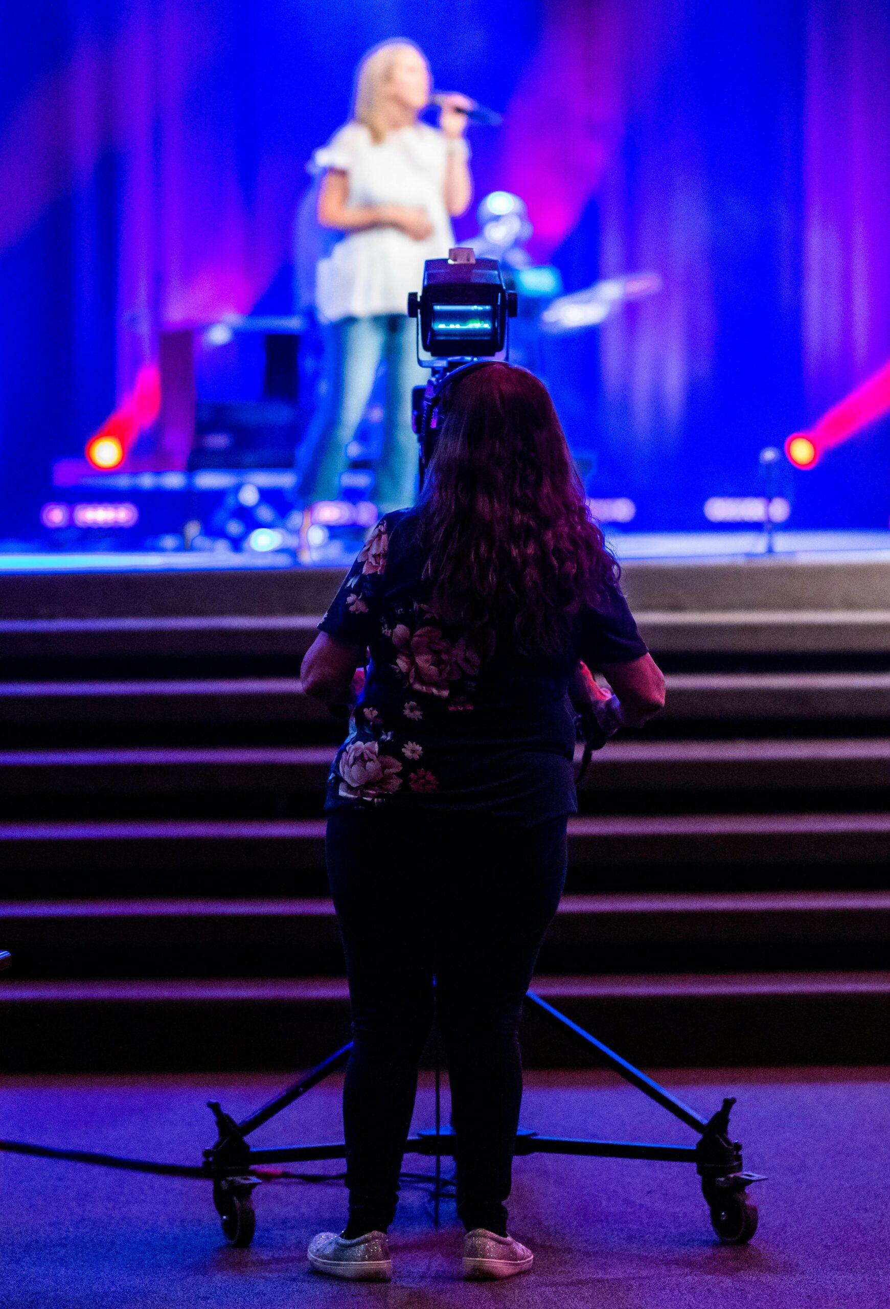 A camerawoman records a live concert on stage, emphasizing production and media.